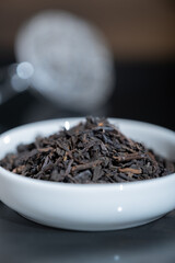 Selective focus closeup of a cup filled with fresh tea leaves. An out-of-focus tea strainer is in the background.