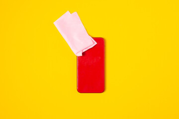 Top view cleaning smart phone screen on yellow background. Flat lay cleaning red phone by fabric microfiber concept