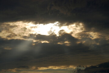 Summer cloudy sky covered with clouds. In the sky, white-gray, slightly blue clouds with white gaps through which the sun's rays break through.