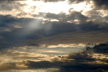 Obraz premium Summer cloudy sky covered with clouds. In the sky, white-gray, slightly blue clouds with white gaps through which the sun's rays break through.