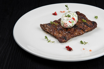 Grilled skirt beef meat steak on a plate with white vegetable sauce decorated by herbs and berries. Dark wooden background