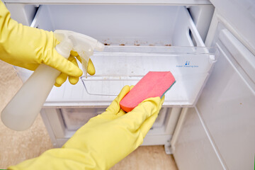 Cleaning the refrigerator freezer from dirt, a male hand in yellow gloves wipes kitchen appliances