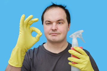 Happy male cleaner showing okay gesture in yellow gloves, portrait on studio blue background