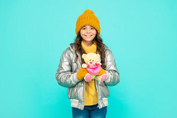 happy kid in puffer jacket and hat. childhood. teen girl hold toy bear.
