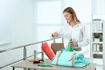 Businesswoman packing sports stuff for training into bag in office