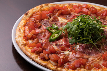 ham pizza with tomatoes, cheese and topped with green chili peppers and arugula