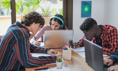 Young multiracial students learning together while using computer laptop and books