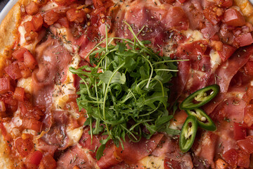 ham pizza with tomatoes, cheese and topped with green chili peppers and arugula