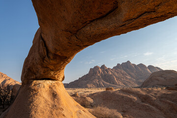 The imposing stone arch in the morning light and in the background the peaks of Spitzkoppe,...