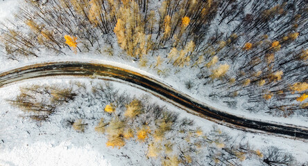 Aerial high angle view of narrow winding curvy mountain road among the trees in winter forest. Snowy landscape, bird's eye view.