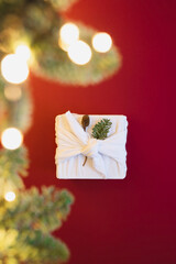 Eco and sustainable gift wrapping ideas. White gift box in cloth on red background. Christmas New Year backdrop with Furoshiki wrap and bokeh lights. Recycling concept and eco-friendly alternatives.