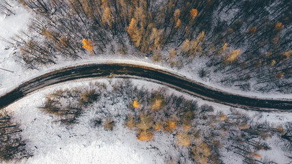 Aerial high angle view of narrow winding curvy mountain road among the trees in winter forest. Snowy landscape, bird's eye view.