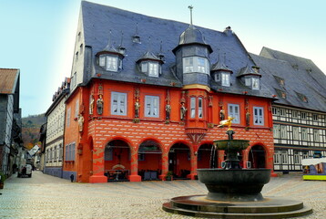 Alter Marktbrunnen vor malerischem rotem Gildehaus auf schönem Marktplatz von Goslar bei blauem...