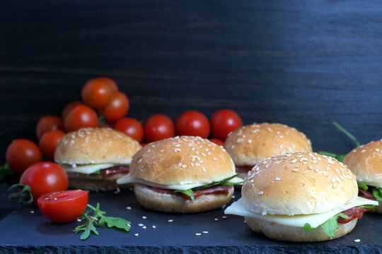 Buns with cheese, ham, herbs and ketchup. Fresh cherry tomatoes and rukula salad. On a dark vintage background