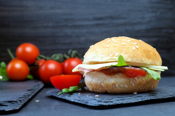 Hamburger with cheese, ham, herbs and ketchup, fresh tomatoes. Close-up