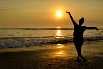 Fototapeta premium Silhouette of a woman with open arms on the shore of a beach at sunset. The golden hour