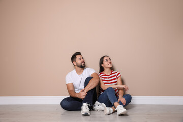 Fototapeta premium Young couple sitting on floor near beige wall indoors