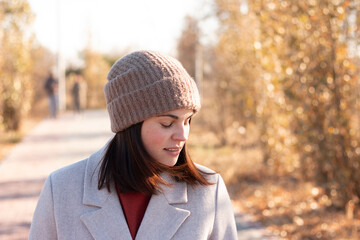 Smiling girl in a knitted hat and coat walks along a paved path in an autumn park