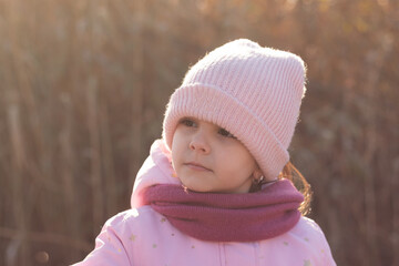 Little girl in a pink winter hat and coat on the background of an autumn landscape