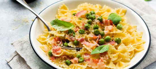 Fettuccine pasta with bacon and green peas and parmesan cheese in light plate on old gray concrete background. Top view.