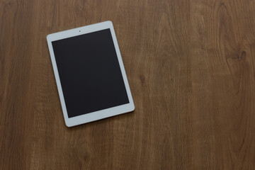 white tablet slightly turned to the left on brown wooden material and slightly displaced to the left &middot; horizontal view