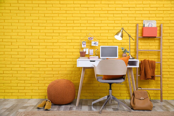 Stylish home office interior with comfortable workplace near yellow brick wall. Space for text