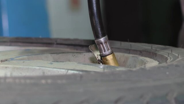 Tire pressure check. Closeup of mechanic inflating tyre with alloy wheel. the refill pressure head and black tyre with alloy wheel at car service shop center
