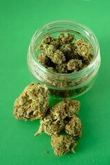 Close up of cbd cannabis buds in glass jar, macro view. Medicinal marijuana blooms on green paper...
