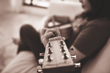 Blur images of woman sitting on sofa and relaxing by playing a guitar, to people and relaxation by music concept.