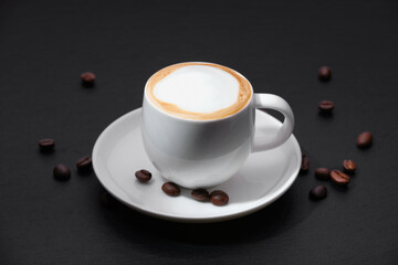 Coffee with coffee beans. White cup of coffee on a black background. A cup of coffee on a textured black table.