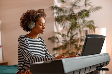 Young multiracial female musician playing melody on electronic musical instrument while spending...