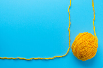 Ball of yellow wool yarn on bright blue background. Knitting, handmade and hobby concept. Flat lay, top view with copy space. - obrazy, fototapety, plakaty
