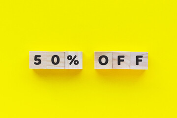 Text 50% OFF on wooden cubes on yellow background. Black friday. Big sale. Square wood blocks. Top view, flat lay.