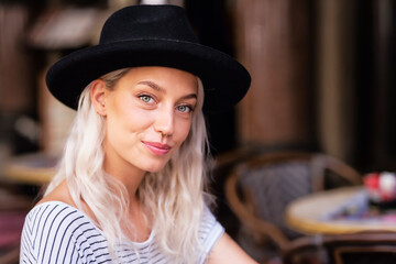 Beautiful stylish woman wearing hat and piercing while sitting at outdoor cafe