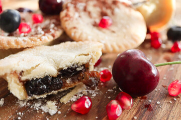 Christmas fruit mince pies with cherries pomegranate seeds raisins and blueberries. Dusted in icing sugar and cocoa powder
