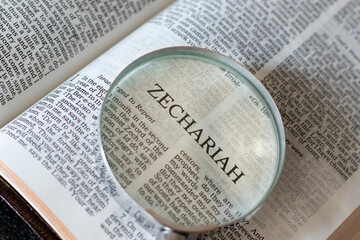 Open Holy Bible Book Zechariah prophet Old Testament Scriptures with a magnifying glass. The...