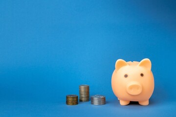 Pink piggy bank and coins on a blue background. Money saving and deposit concept