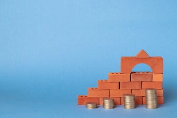 Stacks of coins in the form of steps against a background of blocks of red bricks. Construction investment concept