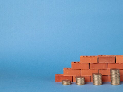 Stacks of coins in the form of steps against a background of blocks of red bricks. Construction investment concept
