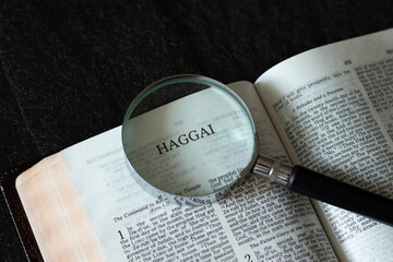 Open Holy Bible Haggai the prophet from Old Testament with a magnifying glass on dark granite background. The Christian biblical concept of studying the Scriptures from God and Jesus Christ.A close-up - Powered by Adobe