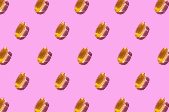 On a light pink background, a pattern of yellow omega 3 capsules. Medical summary. Wallpaper for your phone or canvas