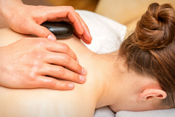 Obraz na płótnie Canvas Hot stone massage therapy. Caucasian young woman getting a hot stone massage on back at spa salon.