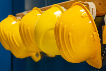Line of new yellow protective helmets for workers hangs on wooden bar in dressing room of...