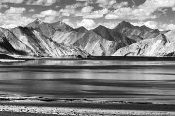 Rocks and reflection of Mountains on Pangong tso (Lake) with blue sky. It is huge lake in Ladakh, extends from India to Tibet. Leh, Ladakh, Jammu and Kashmir, India. Black and white stock image.