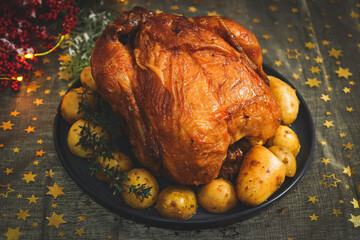 Hot chicken with potatoes in a dish and fir branches with a garland on a table.