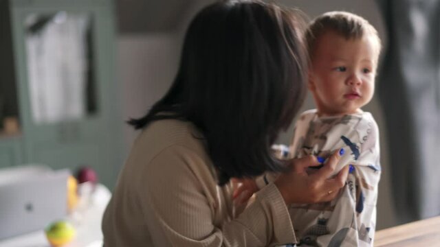 Handsome Asian Mom Soothing And Kissing Her Baby In The Kitchen