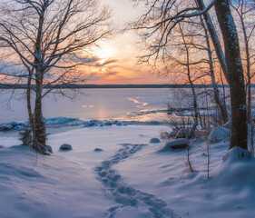 Snow trail to the lake under ice at sunset. Winter landscape.