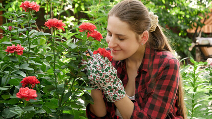 Smiling young female gardener enjoying smelling and looking at her roses in flower garden