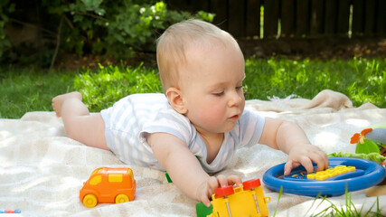 Cute baby crawling on grass to colorful toys. Concept of child early development, education and relaxing outdoors.