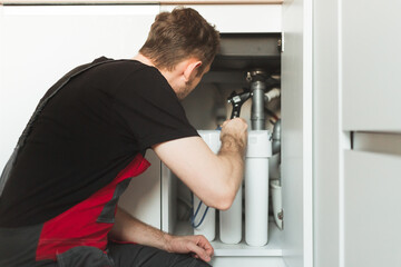 Plumber in the kitchen installs a household water treatment system. Three stage flask system